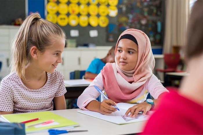 Two girls sitting together drawing in a classroom