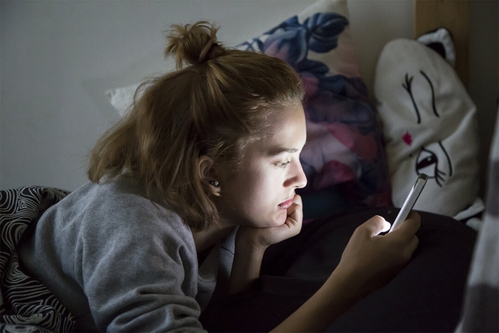 Older girl on bed staring at smartphone