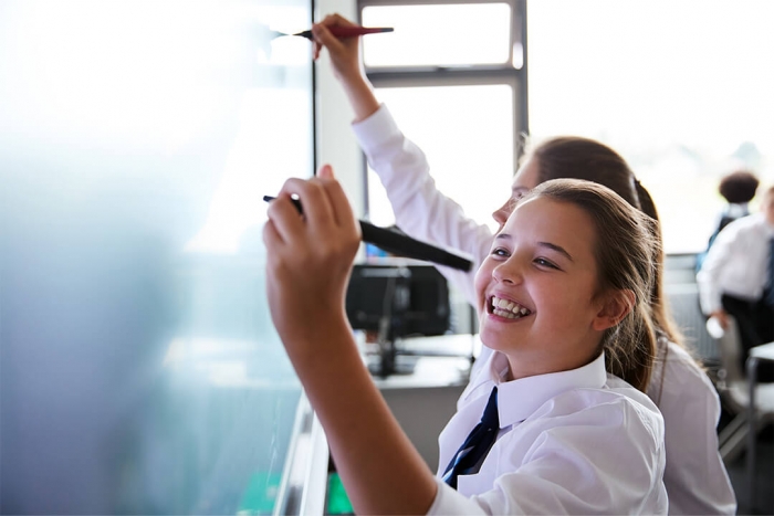 Two smiling girls drawing on an interactive board in classroom